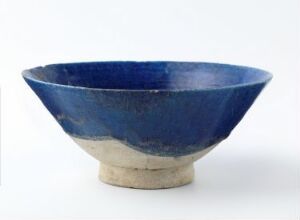  A handmade ceramic bowl with a rich cobalt blue glaze inside and on the upper exterior, transitioning to a natural, unglazed beige ceramic on the lower exterior, set against a neutral background.