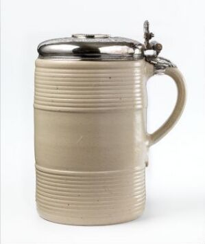  An antique ceramic beer stein with horizontal ridges and a metallic pewter lid, featuring a decorative thumblift, set against a light gray background.