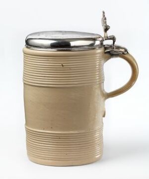  A traditional beige ceramic beer stein with horizontal ridges and a shiny metal lid featuring an ornate thumb lever, set against a plain, light-colored background.