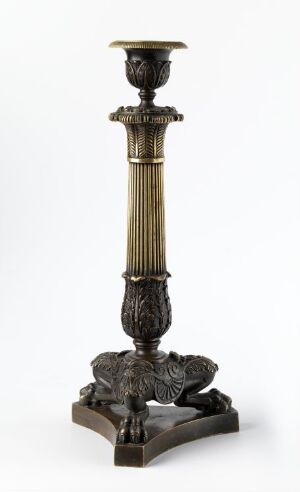  A decorative antique-style metal candlestick with a fluted stem and embellished base, featuring a dark patina and bronze highlights, against a plain background.