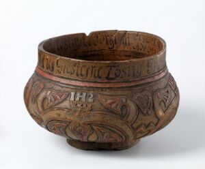  A handcrafted wooden bowl with a red and black patterned band around the top edge, featuring intricate carvings of abstract organic shapes possibly symbolizing traditional motifs.