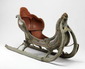  An intricately crafted antique "Spisslede" sled by Peder Pedersen Aadnes, featuring a reddish-brown leather seat with embossed designs, set within a greenish-gray painted wooden frame with red, black, and gold accents and decorative carvings, completed with sturdy wooden runners bound by metal.