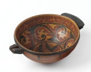  An ancient ceramic bowl with two handles, featuring intricate red-brown, golden yellow, and dark green floral designs inside the rounded basin, set against a light grey background.