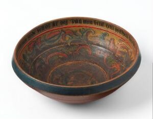  An ancient-style ceramic bowl with a wide rim and intricate designs in muted green, orange, red, and faint blue on the interior, featuring a band of faded inscriptions around the upper part of the bowl, set against a light background.