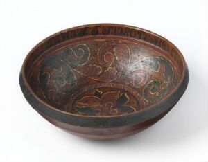  An ancient ceramic bowl with intricate cream or light tan designs on a deep reddish-brown background, suggesting traditional craftsmanship, possibly with historical significance. The bowl's wide shape and slightly out-turned rim enhance its traditional aesthetic.