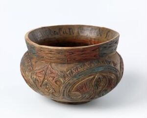  An earthenware bowl with tribal-like etched patterns in various shades of brown and terracotta, featuring a small foot for standing and a darker, burnished interior.