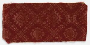  A fragment of an antique textile with a deep maroon background showcasing a repetitive geometric pattern in a slightly lighter shade, displaying traditional octagonal and diamond shapes with small crosses and angular motifs.