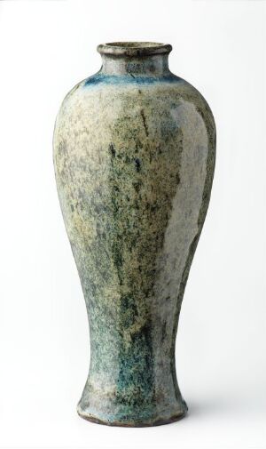  A tall ceramic vase with a flaring rim and a textured surface, transitioning from deep cobalt blue at the top to greenish-gray in the middle and hints of blue at the bottom, set against a white background. The vase has an antique quality with a patina simulating aging or mineral deposits.