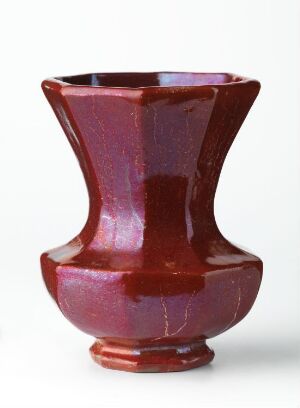 
 A glossy red ceramic vase with a flared rim, constricted neck, and bulbous body on a small circular foot, against a plain white background.