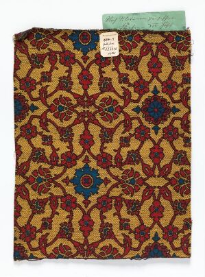  An ornate piece of fabric with a deep brown background and a repetitive golden-yellow floral motif pattern, accented by red, blue, and green colors, with a library or archive tag at the top.