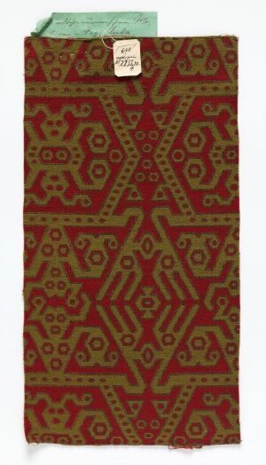  A long piece of fabric with a traditional maroon and gold geometric pattern, possibly indicative of artisanal textile work, with a tag attached to the top edge.