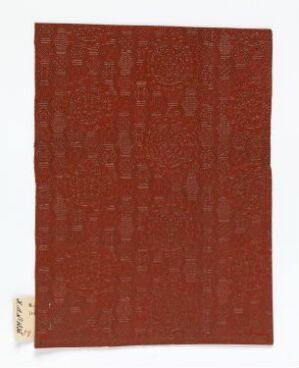  A textured artwork predominantly in deep red tones with variations of maroon and orange suggests a tactile, organic surface. A small, rectangular gallery label is affixed to the bottom right corner. The artist name and title of the piece are unknown.