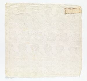  An image of an aged and blank piece of paper or fabric with frayed edges and a small, yellowed label in the top right corner, indicating possible historical or archival use.