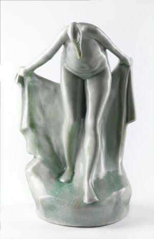  A porcelain sculpture titled "Birdy" by Irene Nordli, depicting a serene, slender nude female form with arms raised and hands joined above her head, suggesting the beginnings of wings, glazed in soft shades of green with a gentle sheen.