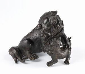  A small bronze figurine of a Chinese guardian lion or 'Foo Dog' in a playful pose with a detailed mane and expressive face, made from a lustrous metallic material with a dark finish.