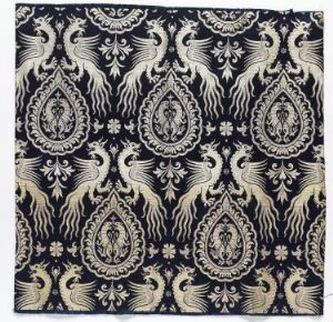  A square of black fabric with a repetitive paisley and bird pattern in white and gold, showcasing a traditional and elegant design.