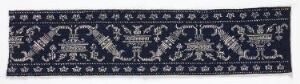  A rectangular textile fragment with a dark navy blue background featuring a symmetrical creamy white and beige floral and vine pattern, suggesting a historical or traditional design, possibly used as a decorative border. Artistname and title remain unknown.