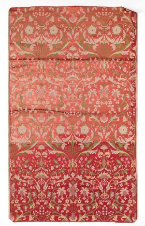  A photograph of a fabric with a detailed floral pattern in shades of red, pink, and cream, featuring intricate and symmetrical designs reminiscent of traditional Middle Eastern or South Asian textiles.