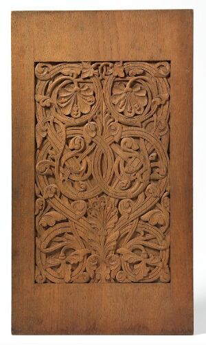  An intricate floral-patterned wooden carving panel set within a simple wooden frame, showcasing a rich variety of brown tones and the three-dimensional relief effect of the stylized roses and foliage. Artist and title unknown.