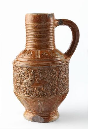  A detailed, terracotta-colored ceramic pitcher with a ridged neck and embossed designs featuring figures in a historical or mythological setting, with a sturdy handle and flat base.