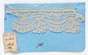  A piece of white lace with intricate floral design laid out on a pastel blue background, accompanied by a small aged paper label with handwritten text.