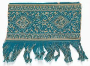  An ornate deep teal textile with intricate gold and darker teal scrollwork patterns and stylized foliage designs, finished with a teal fringe on one end. Artist name and title are unknown.