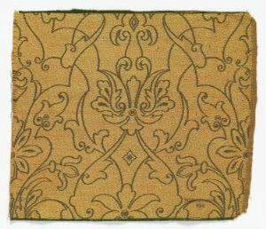  A fragment of fabric with a symmetrical floral pattern in shades of sandy and darker brown, evoking a traditional or historical aesthetic. The design features curvilinear shapes and a stylized central fleur-de-lis motif.