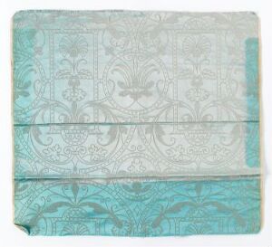  A square piece of aged aqua or turquoise fabric or paper with a symmetrical decorative pattern featuring traditional scrolls and floral designs, showing signs of wear and a horizontal fold across the middle.