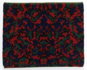  A piece of fabric featuring a symmetrical pattern of bright red and green floral designs on a deep, dark blue background with soft fraying at the edges, indicative of a traditional textile. Artistname and title are unknown.