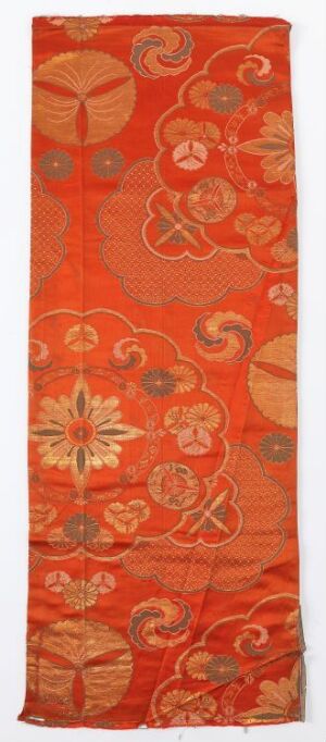  A tall, narrow, orange-red textile with an intricate pattern of stylized flowers and scrollwork, suggestive of traditional silk weaving.