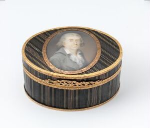  A round ebony container titled "Dåse" by F. Toselli, adorned with vertical striped patterns, a central portrait medallion, and embellished with engraved and chiseled gold and silver edges on a light background.