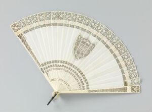  An antique, ivory-colored handheld fan with intricate geometric and floral patterns in soft gray or pale gold, featuring a darker crest design on the right side, displayed against a neutral background.