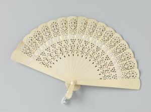  An elegant ivory-colored handheld folding fan with delicate openwork patterns and a scalloped edge, displayed against a light grey background.