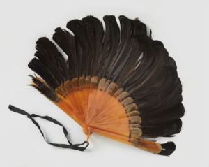  A traditional folding fan with wood or bamboo ribs and feathers in a gradient of black, brown, and cream, resting against a white background with a black cord attached to the base.