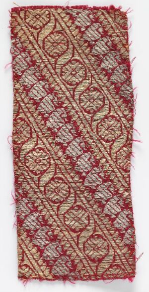  An embroidered textile fragment with a faded red background, featuring a golden and light-colored symmetrical vine-like pattern, demonstrating intricate craftsmanship and possibly antique in nature.