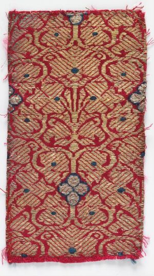  A rectangular fragment of antique fabric with a detailed red and golden-yellow symmetrical design, featuring a central floral motif and minor blue and green accents, frayed edges, and signs of wear.