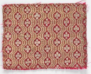  A textile with a repetitive octagonal pattern in dark red against a warm beige background, featuring minute floral and geometric designs in shades of red, pink, and light green.