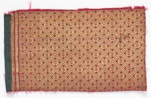  A detailed textile featuring a beige background with a repeating pattern of reddish-brown diamond shapes, with narrow horizontal borders and fringed edges that have threads in red and pink.