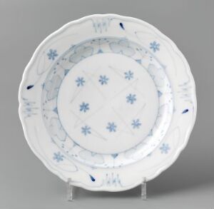  A white feldspar porcelain plate titled "Blaaveis" by Gerhard Munthe, showcasing hand-painted and stencil-painted underglaze decoration of delicate blue flowers and patterns, with an embossed rim suggesting a folded fabric design, set against a neutral background.