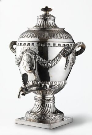  A polished silver classical urn with ornate handles and embossed decorative motifs stands against a neutral background, reflecting a sense of historical elegance.