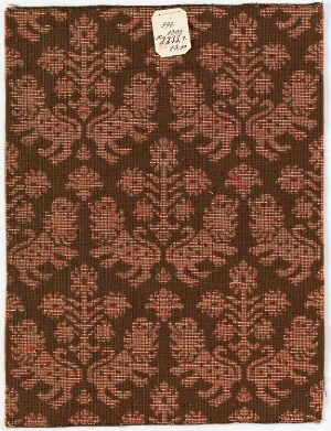  A warm brown surface with a repetitive, symmetrical pattern of stylized terracotta floral motifs, and a small white label in the top left corner with handwritten code, suggesting a vintage or historical patterned material.