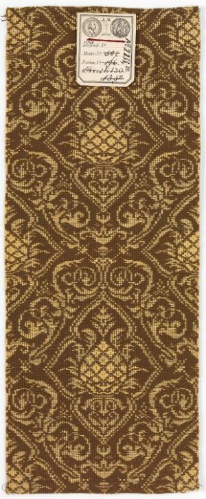  An ornate, rectangular brown and gold textile with a symmetrical pattern featuring diamond-shaped motifs, floral elements, and intricate scrollwork, with a label at the top center.