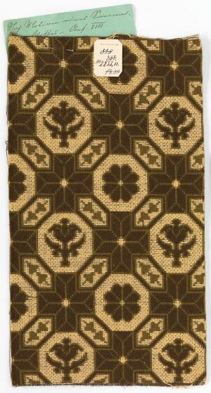  A rectangular fabric or paper piece with a traditional pattern featuring golden brown clover and fleur-de-lis motifs on a dark brown background, with a small label in the top left corner. Artist's name and title unknown.