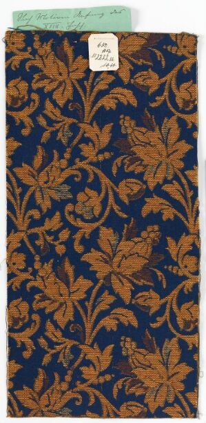  Vertical sample of patterned fabric or wallpaper with intricate gold and ochre floral designs on a deep blue background, possibly historical, with a label attached to the top edge. Artist and title are unknown.