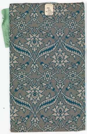  A fabric swatch featuring a symmetrical botanical print with stylized flowers and leaves in shades of gray-blue, white, and teal, with a label attached in the upper right corner.