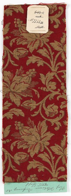  A sample of fabric or wallpaper with a traditional floral pattern in dark burgundy on a deep red background, with two informational labels attached to it.