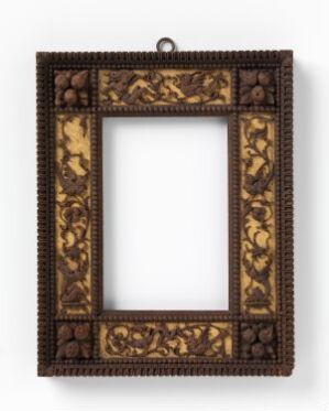  An empty antique picture frame with intricate gold-leaf patterns against a dark wooden backdrop, featuring carved acanthus leaves and beaded motifs, suggesting a baroque or rococo style.