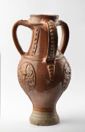  An ancient-style terracotta pitcher with embossed medallions and ridged handles, exhibiting a reddish-brown color with subtle variations in hue and light across its textured surface. Artistname and title are unknown.