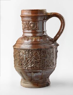  Traditional ceramic jug with a rich brown glaze and intricate embossed decorations, featuring a single handle and a detailed relief scene on the main body, against a light gray background.