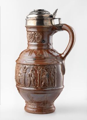  An ornate stoneware beer stein with a silver-toned metal lid and thumb lever, featuring a raised relief design with historical or allegorical figures in earthy brown and tan colors.